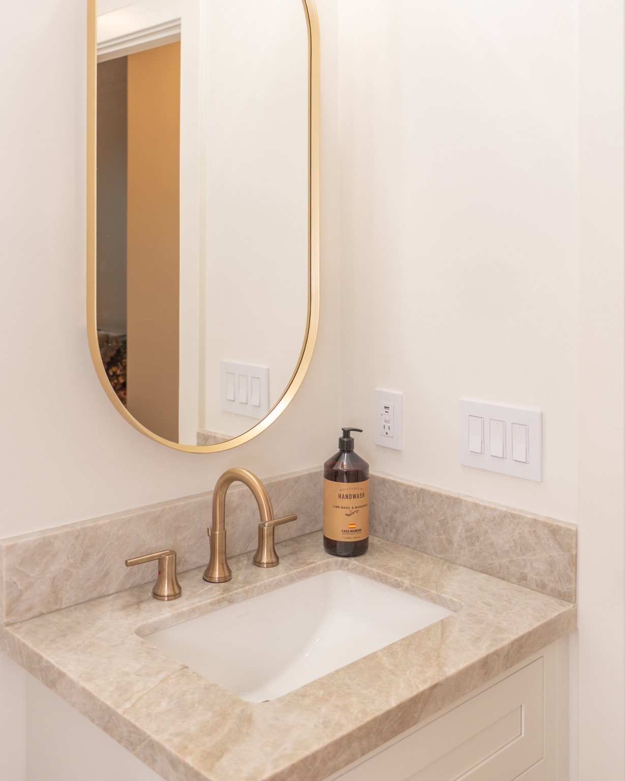 Completed powder room with brass fixtures and an oval storage mirror