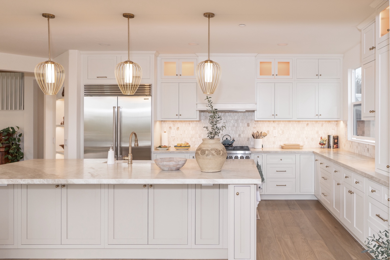 White kitchen with a stone island, shaker cabinetry and brass pendants
